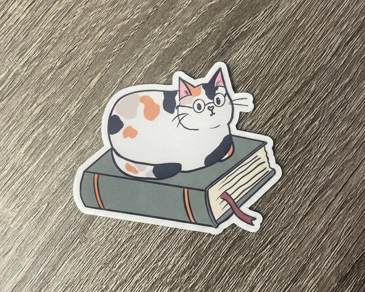 Sticker of a cat sitting on a book on a wooden surface