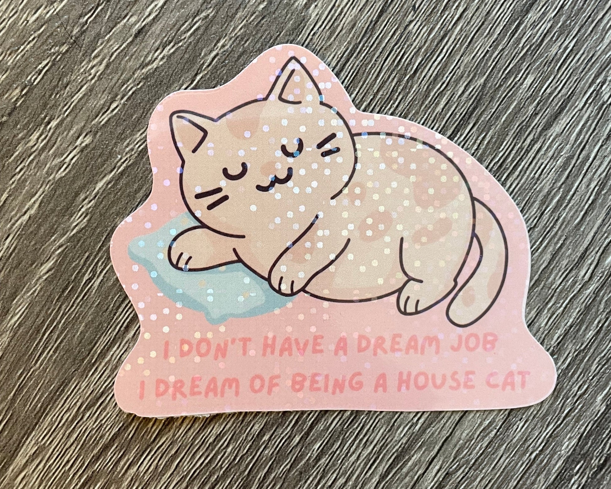 Sticker of a cat lying on a cloud with text on a wooden surface